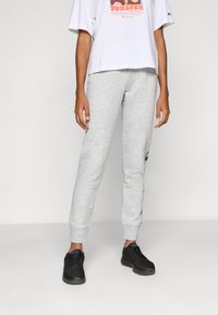 Pantaloni della tuta grigi in cotone con design aderente, caviglie cuffiate e logo laterale. Abbinati a una t-shirt grafica bianca oversize e sneaker nere.