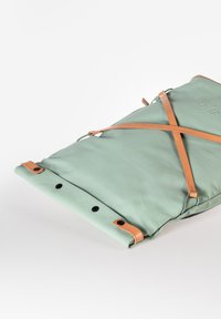 Borsa di tessuto verde con manici in pelle marrone, caratterizzata da un design pieghevole e bottoni a pressione. Texture liscia con dettaglio di branding minimalista.