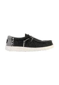 Zapato slip-on de tela gris con una suela blanca moteada, que presenta una parte superior texturizada, cordones y adornos decorativos en el lateral.