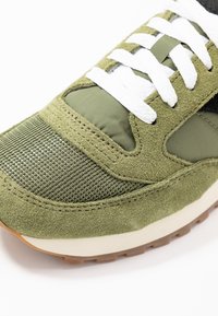 Oliivinvihreät tennarit, joissa on yhdistelmä texturoitua mokkaa ja verkkopaneeleja, valkoiset nauhat ja vaaleansävyinen kumipohja, jossa on pitovoimaa.