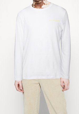 Weißes Langarm-T-Shirt mit rundem Ausschnitt und kleinem gelbem "HILFIGER"-Logo auf der linken Brust. Weicher Baumwollstoff, taillierte Silhouette.