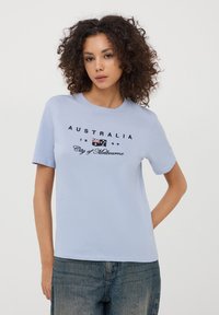 Jasnoniebieska bawełniana koszulka z krótkim rękawem, z czarnym nadrukiem graficznym "AUSTRALIA 1999 Miasto Melbourne" z detalem flagi.