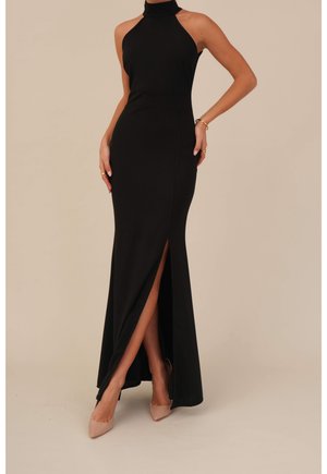 Schwarzes Maxikleid mit Neckholder, figurbetonter Silhouette, Seitenschlitz und glatter Textur. Kombiniert mit hautfarbenen spitzen High Heels.