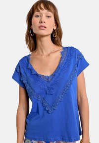 Camiseta de manga corta azul con escote en V profundo, con detalles de encaje a lo largo del cuello en un patrón texturizado. Tecido suave.