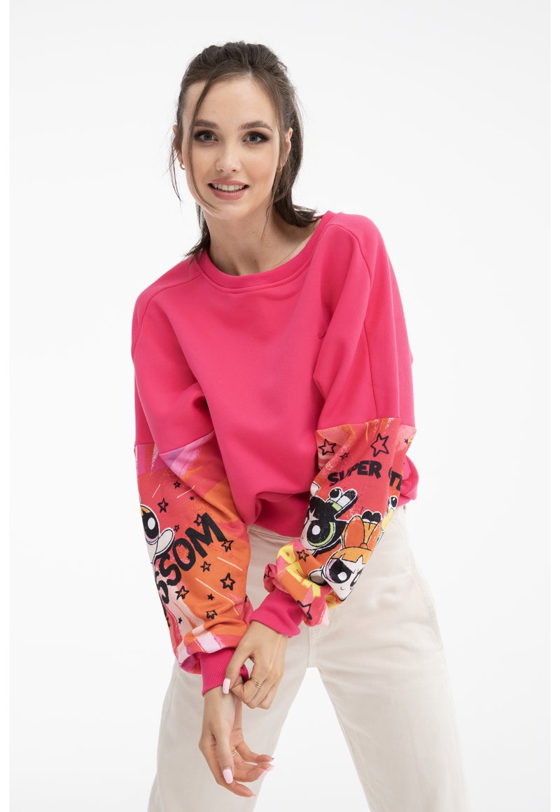 Ružová mikina s farebnými, vzorovanými rukávmi s kreslenými postavičkami a textom. Mäkka látka, voľný strih a rebrované manžety.