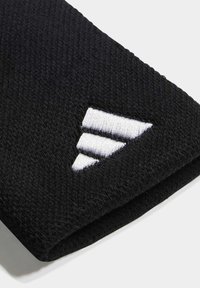 Crni pleteni materijal s teksturiranim završetkom, sa bijelim izvezenim logotipom koji se sastoji od tri dijagonalne pruge na jednom rubu.