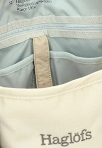 Dettaglio dell'interno di uno zaino Haglöfs grigio chiaro che mostra molteplici tasche cucite e un anello in tessuto beige.