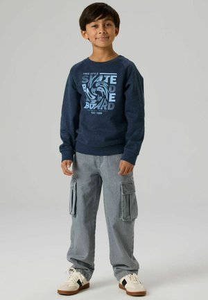 Navy blue sweatshirt with graphic print, paired with light gray cargo pants featuring side pockets, and white sneakers with brown accents.