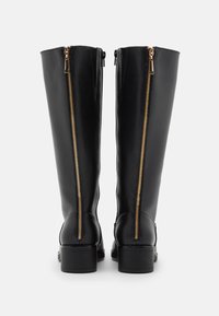 Botas de couro pretas até ao joelho com fechos laterais, hardware em tom dourado e um salto baixo em bloco. Textura lisa com detalhes de design mínimos.