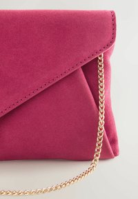 Fuchsiafarbene Clutch aus Wildleder mit dreieckiger Klappe, einem goldenen Kettenriemen und sauberen Nähten entlang der Kanten. Glatte Textur, kompakte Form.