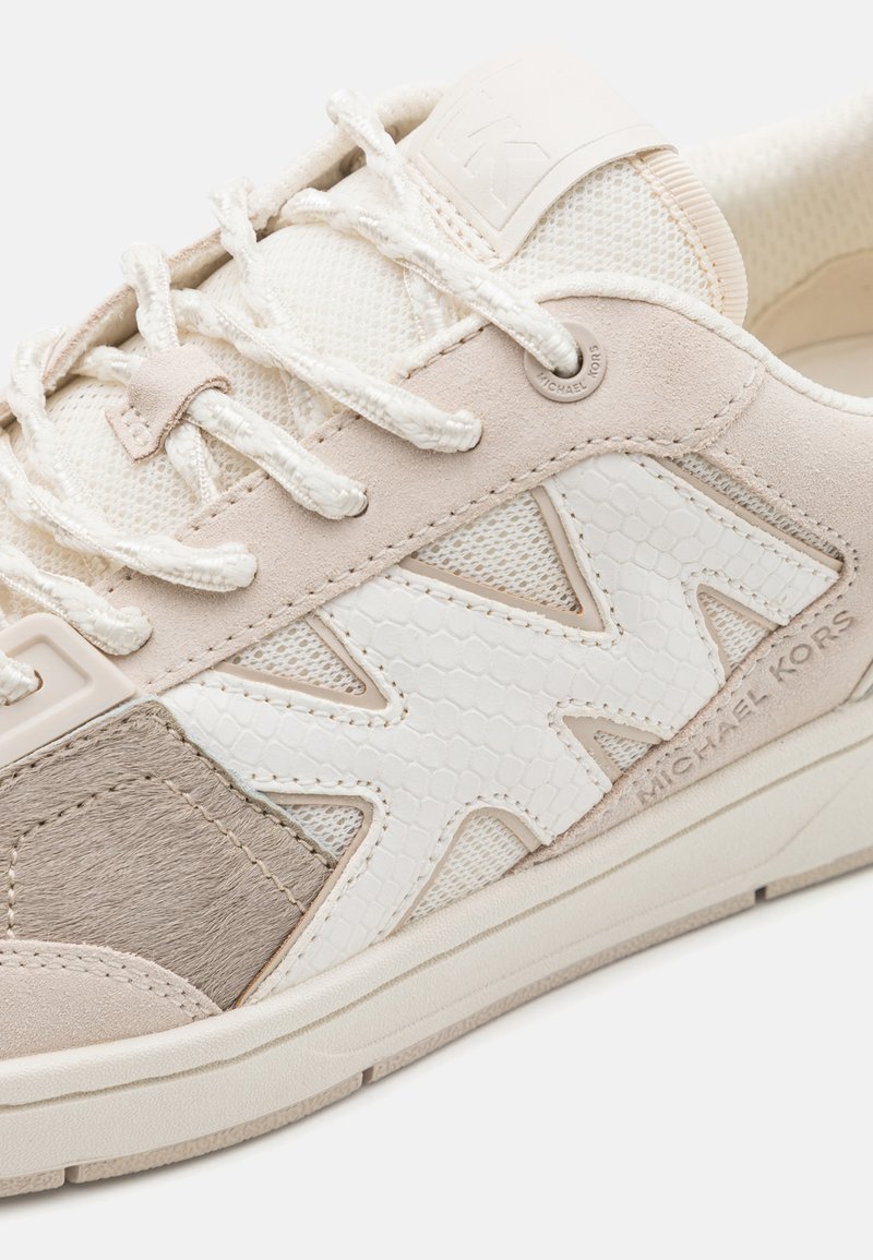 Sneakers beige chiaro con dettagli in rete, suede e un accento bianco testurizzato. Il logo distintivo e i lacci aggiungono un tocco di stile al design sportivo.