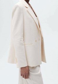 Blazer crème clair avec une coupe ajustée, des revers crantés, deux boutons et une poche poitrine unique ; conçu dans un tissu lisse et léger.