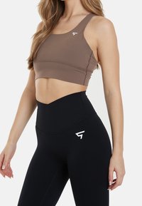 Brun sport-bh med en slät yta och logotyp. Höga svarta leggings med en elegant design och vit logotypdetalj på låret.