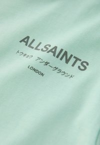 Mintgrønt stof med teksten "ALLSAINTS" og "LONDON" i fed sort print, med asiatiske tegn nedenunder. Glat tekstur, afslappet design.