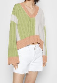 Lichtgewicht, cropped sweater van gestructureerde, geribbelde stof met een V-hals, in groene, perzikkleurige en grijze kleurvlakken. Draagt bij witte shorts.