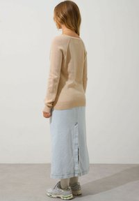 Helles beige Strickpullover mit langen Ärmeln, kombiniert mit einem hellblauen Jeans-Midirock mit einem Schlitz hinten. Getragen mit grauen Sneakers.