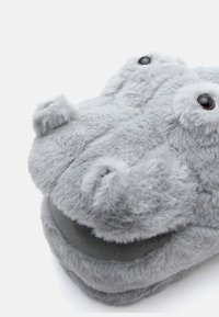 Harmaat pehmeät tossut, jotka on muotoiltu hippopotamuksen muotoon, joissa on pehmeä turkistyyppinen pinta, pyöreä muoto ja mustat nappisilmät päällä.