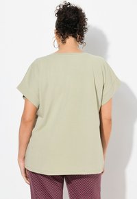 Camiseta verde oliva de manga corta con corte relajado y escote redondeado, combinada con pantalones estampados en rojo y negro.