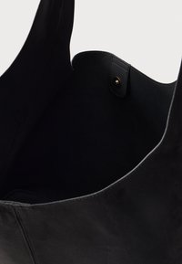 Svart läder tote-väska med mjuk textur, öppen topp och guldknappstängning. Innerväskan är rymlig, ofodrad med en ren design.