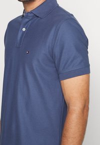 Polo bleue marine en tissu doux, avec col et manches courtes. Présente un petit logo sur la poitrine. Fabriqué en tissu respirant.