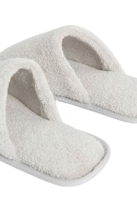Zapatillas de tela de rizo de color crema suave, con diseño de punta abierta y suela acolchada. Presenta una parte superior texturizada y un ribete gris.