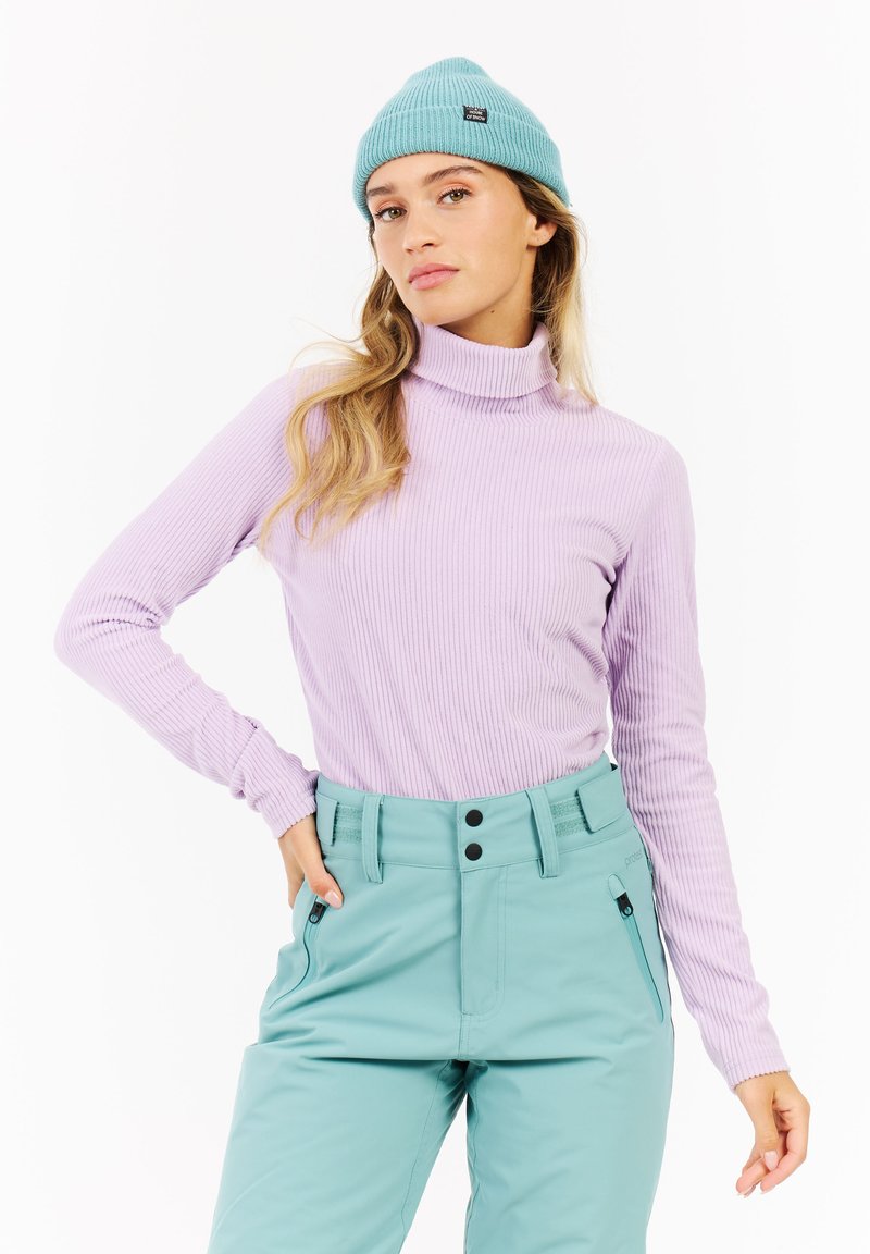 Pull à col roulé violet côtelé et pantalon taille haute vert menthe avec des boutons noirs et des poches zippées. Bonnet en bleu clair.