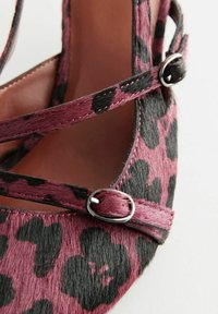 Leopard print flat shoe in pink and black, featuring a soft textured surface, crisscross straps, and silver-tone hardware accents.