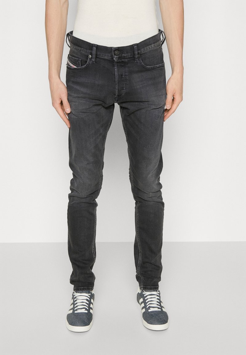 Slim-fit black denim jeans with subtle fading, five-pocket design, and contrasting stitching. Paired with gray athletic shoes.