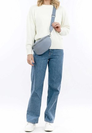 Ljusblå läderväska med korsrem och rundad form, dragkedja, justerbar rem och texturerad yta, bärs av en person i vit tröja.