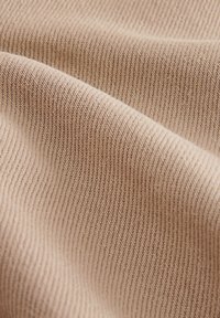 Beige gebreide stof met een geribbelde textuur, voorzien van fijne verticale lijnen en een zachte uitstraling. Het valt soepel en toont zachte rondingen.