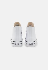Zapatillas altas de cuero blanco con suelas de goma negra, acentos en blanco y negro, y parche de logo circular en la parte trasera.