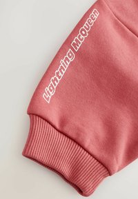 Manche de sweat-shirt rose avec poignet côtelé et texte blanc "Lightning McQueen" imprimé près du poignet.