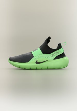 Sneaker Nike slip-on nero e verde neon con cinturino elastico, testo "Just Do It" e logo swoosh su uno sfondo chiaro e semplice.