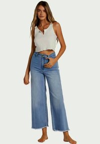 Top cropped branco leve com nervuras e bainha arredondada, combinado com jeans de corte largo azul desbotado com bainha crua e cintura alta.