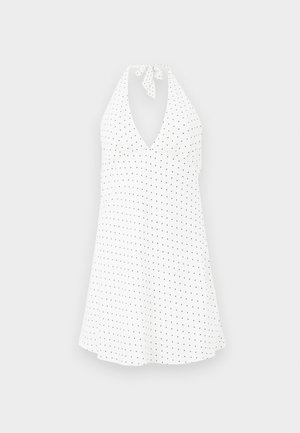 Witte halterjurk met een diepe V-hals, voorzien van een strik bij de hals en zwarte stippen. Vloeiende stof met een licht gebogen zoom.