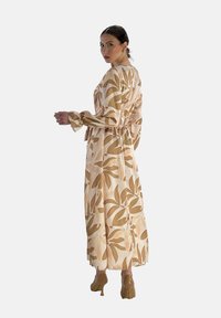 Robe à manches longues avec un motif floral en crème et en tons terreux, présentant une taille cintrée et des manches évasées, avec une silhouette fluide.