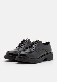 Chaussures à lacets en cuir noir brillant avec détails en clous dorés et semelles épaisses, vues de côté sur fond blanc.