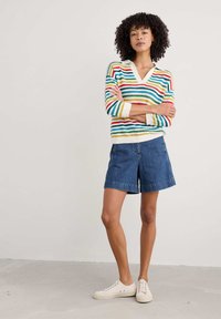 Pull rayé multicolore avec un col en V, assorti à un short en denim bleu. Le pull présente des rayures horizontales en rouge, vert et jaune.