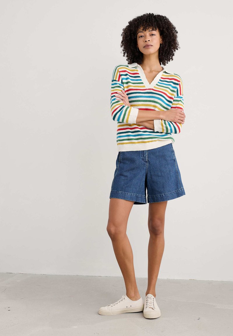 Suéter a rayas multicolor con escote en V, combinado con pantalones cortos de mezclilla azules. El suéter presenta rayas horizontales en rojo, verde y amarillo.