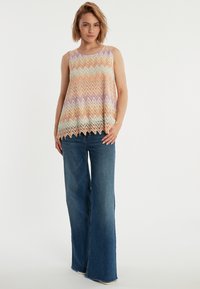 Mouwloos shirt met een zigzagpatroon in pastelkleuren van oranje, lavendel en muntgroen; losse pasvorm; gecombineerd met wijde denim jeans.