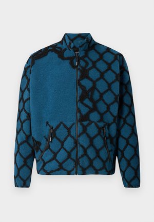 Blue fleece jacket with a black geometric pattern, full zip front, high collar, and two zippered side pockets. Soft texture throughout.