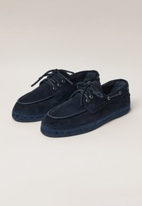 Navy suede shoes with a woven sole, round toe, and lace-up design. Features metal eyelets and visible stitching along the edge.