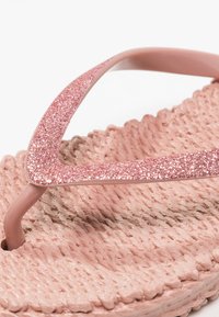 Gros plan d’une tongs rose avec des brides pailletées et une semelle tissée texturée.