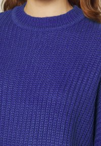 Lila ribbad stickad tröja med rundad halsringning, som har en strukturerad yta och en avslappnad passform.