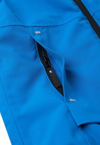 Tessuto blu con una superficie liscia presenta una tasca con zip nera parzialmente aperta e un piccolo accento argentato vicino alla cucitura.