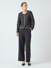 Giacca nera con texture, colletto rotondo e bordi a contrasto crema, abbinata a pantaloni neri a gamba larga e scarpe nere con punta.