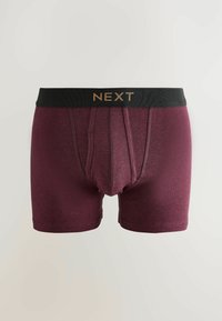 Boxer da uomo bordeaux con elastico nero in vita che presenta la scritta "NEXT" in lettere dorate, disposti in piano su uno sfondo chiaro e semplice.