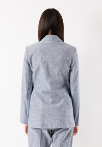 Blazer grigio chiaro con finitura testurizzata, caratterizzato da un singolo spacchetto posteriore e rever a punta. Vestibilità su misura con maniche lunghe e un aspetto liscio.