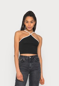 Top halter cropped preto com acabamento branco, apresentando um design exclusivo com alças cruzadas. Combinado com jeans escuros de cintura alta.