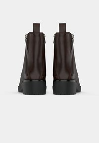 Brązowe skórzane botki za kostkę z teksturowanym wykończeniem, bocznymi suwakami i solidną czarną gumową podeszwą. Posiadają uchwyt z tyłu.